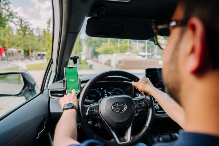 Kierowca Bolt za kierownicą, aplikacja Bolt na telefonie w uchwycie